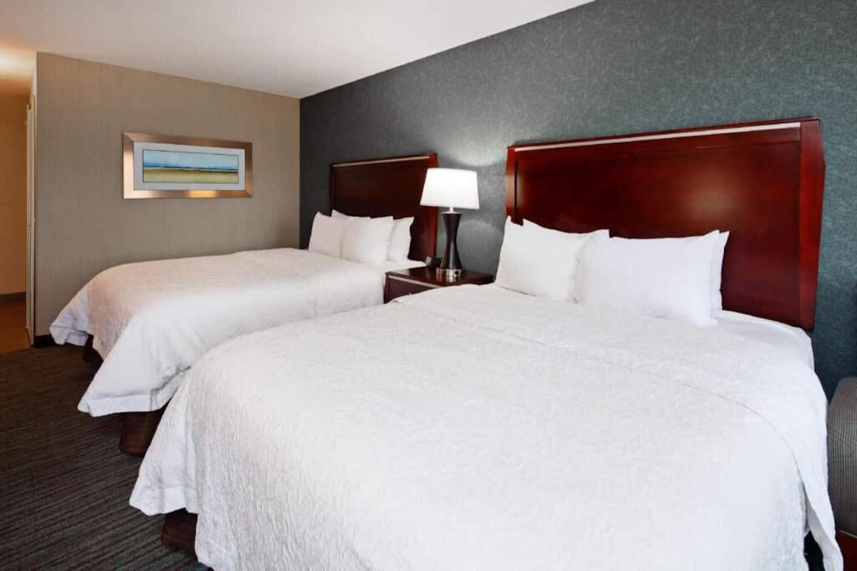 A hotel room with two beds, a nightstand with a lamp, a framed picture on the wall, and a carpeted floor.