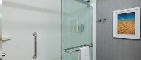 A modern bathroom with a glass shower enclosure, a glass towel rack, and a framed artwork on the wall.