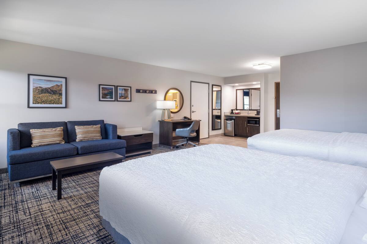 A hotel room with a large bed, a sofa, a desk with a chair, a small bathroom, and framed pictures on the wall.