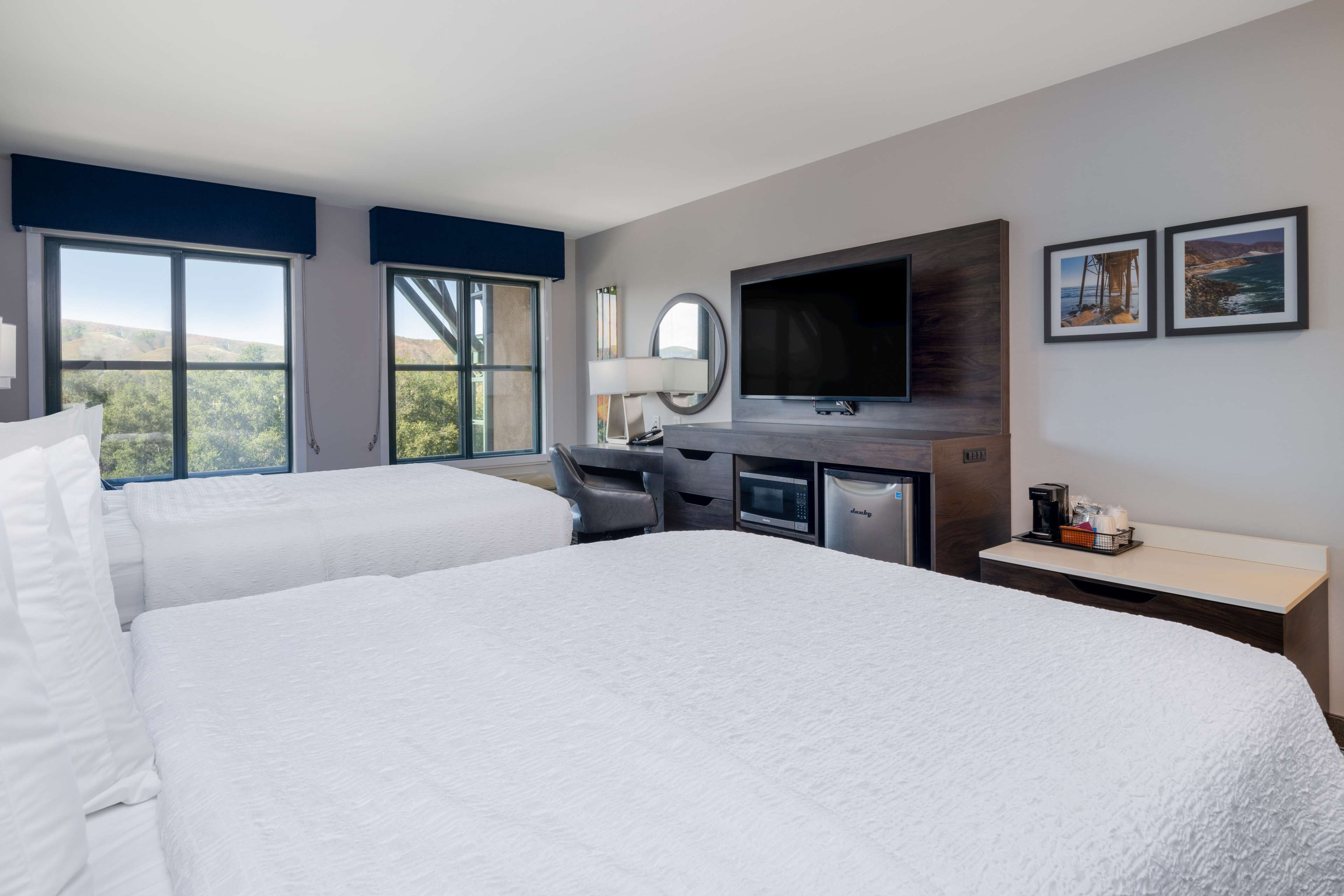 A hotel room with two beds, a desk, a TV, and a coffee maker.