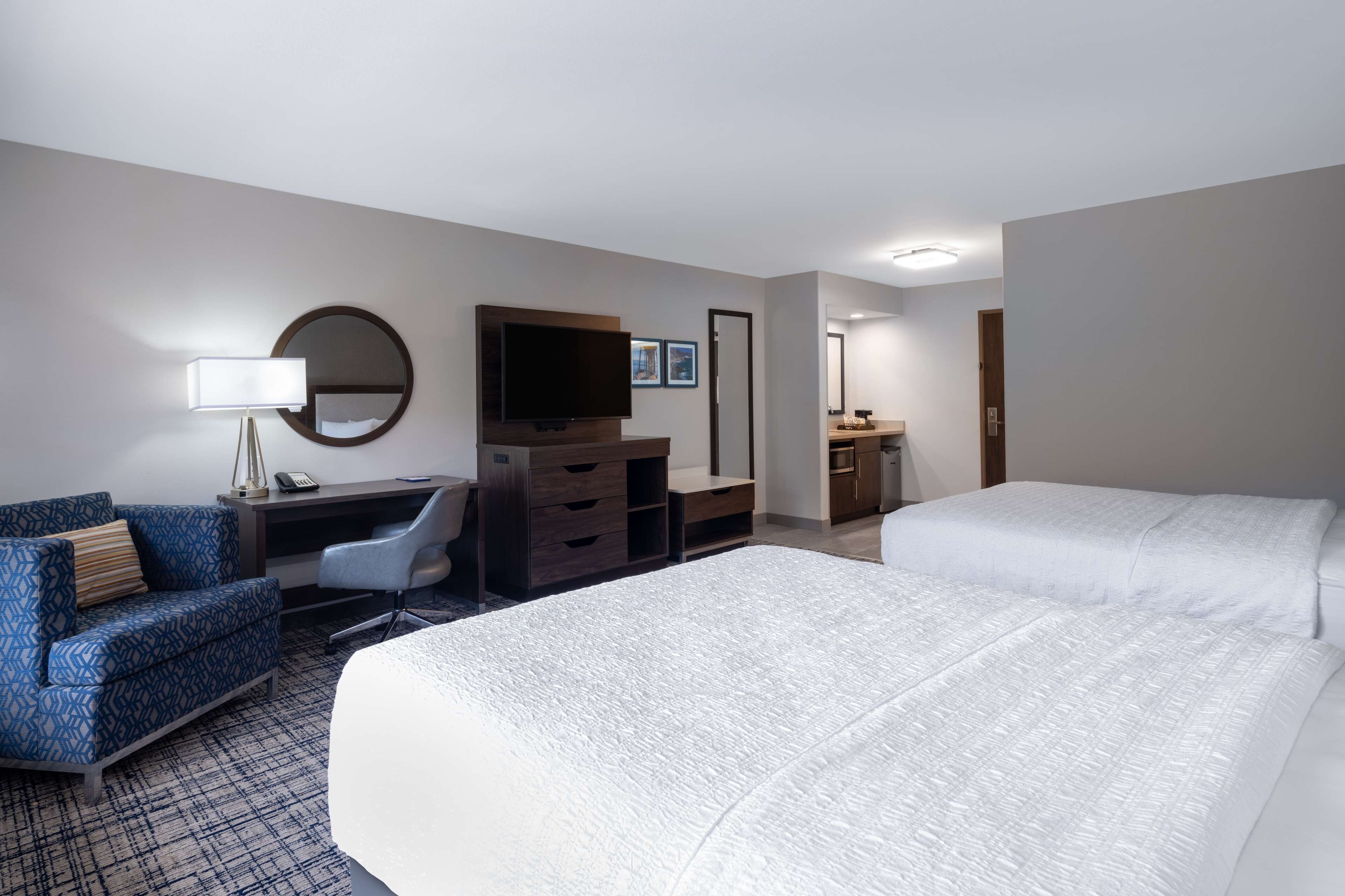 Una habitación de hotel con una cama grande, un escritorio con silla, un televisor, un espejo y un aparador.