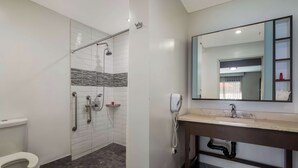 A bathroom with a toilet, a shower with grab bars, a sink with a mirror, and a telephone. - Sunset West Hotel, Surestay Collection By Bw (Los Angeles)
