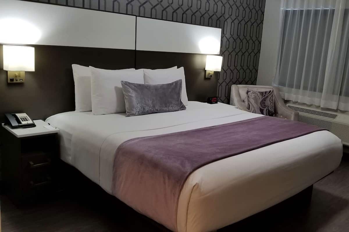 A hotel room with a bed, bedside lamps, a telephone, and a radiator.