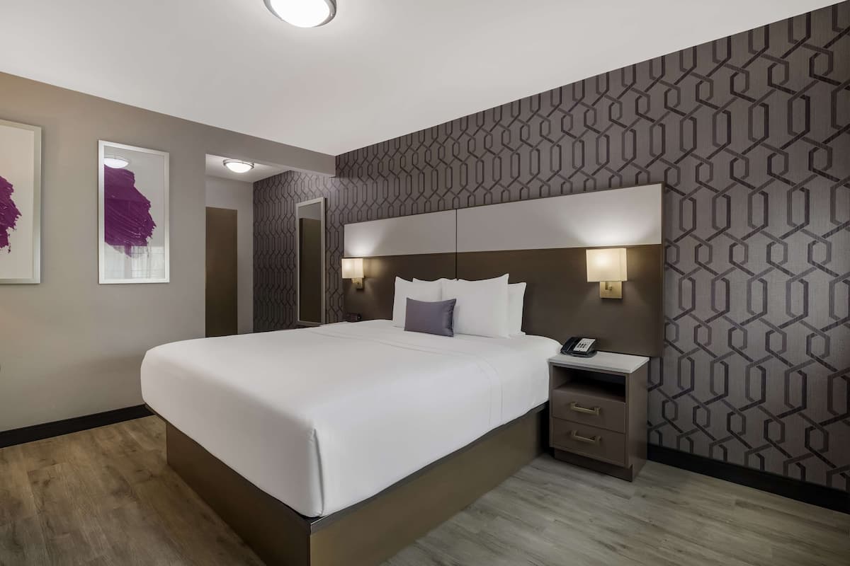 A modern hotel room with a large bed, bedside tables, and a patterned wall.