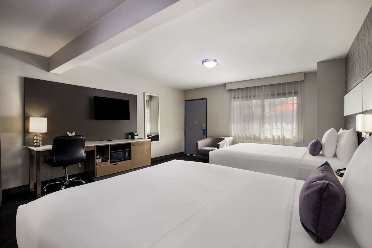 A hotel room with two beds, a desk with a chair, a television, and a window with curtains.