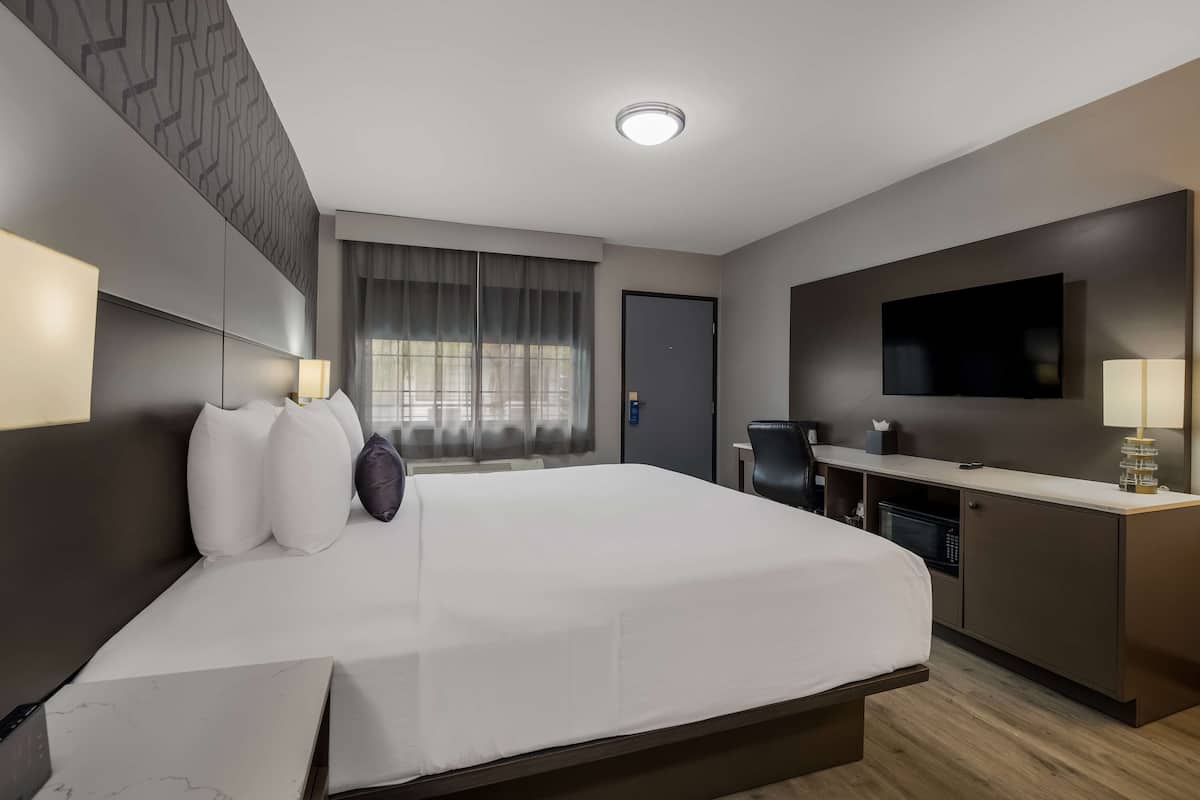 A modern hotel room with a large bed, a desk, a flat-screen TV, and a microwave.