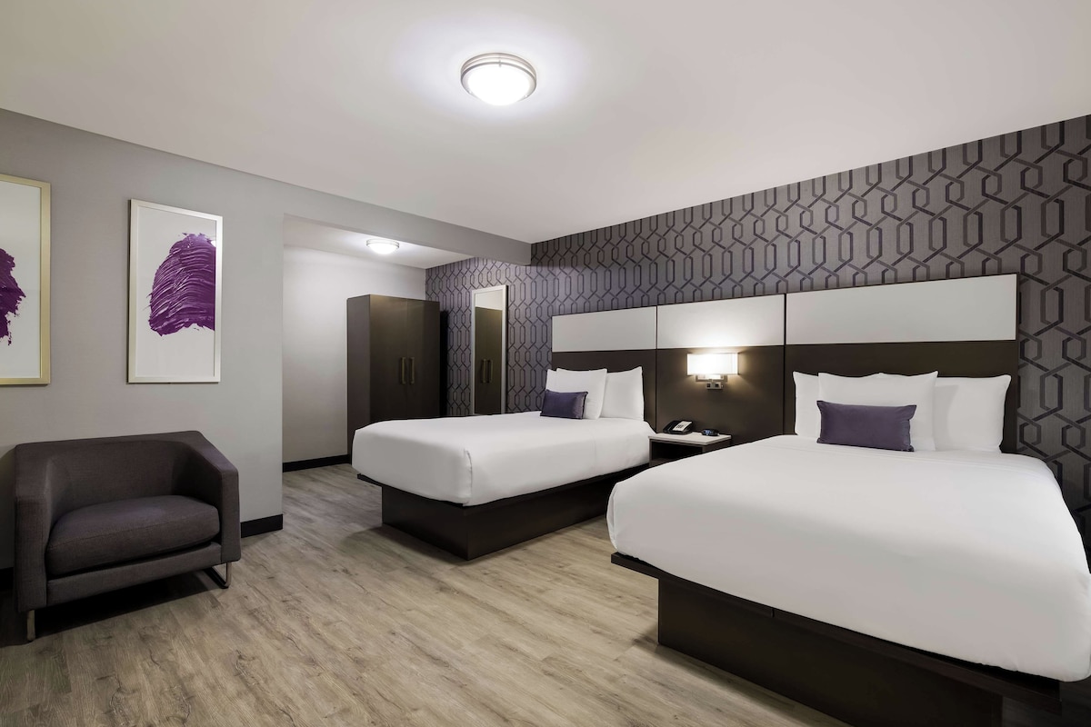 A hotel room with two beds, a sofa, a mirror, and artwork on the wall.