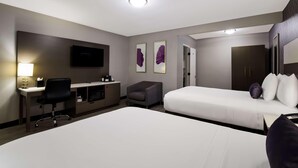 A hotel room with a bed, desk, chair, TV, artwork, and a door. - Sunset West Hotel, Surestay Collection By Bw (Los Angeles)