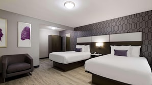 Habitació d'hotel amb dos llits, un sofà, un mirall i obra d'art a la paret.