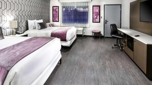 Ein Hotelzimmer mit zwei Betten, einem Schreibtisch, einem Sessel, einem Fernseher und einer Tür.
