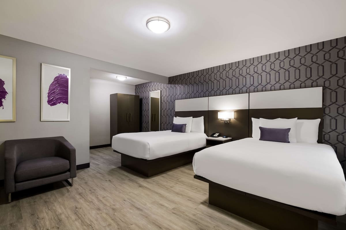 A hotel room with two beds, a sofa, a mirror, and artwork on the wall.