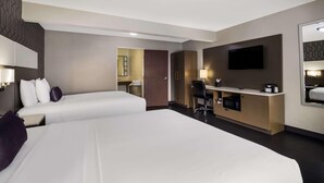 A hotel room with two beds, a desk with a chair, a television, and a microwave. - Sunset West Hotel, Surestay Collection By Bw (Los Angeles)