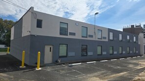 Un edificio moderno con facciata piatta, numerose finestre e un parcheggio delimitato da dissuasori gialli.