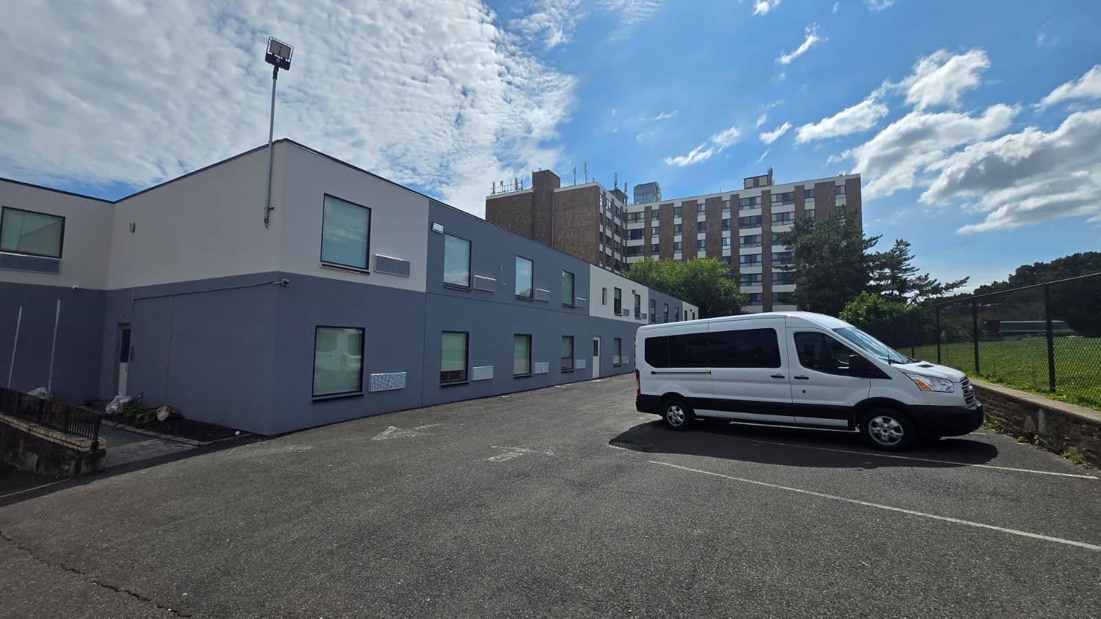 A parking lot with a white van parked in front of a modern building with multiple windows and a flat roof.