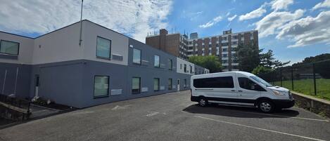 A parking lot with a white van parked in front of a modern building with multiple windows and a flat roof.