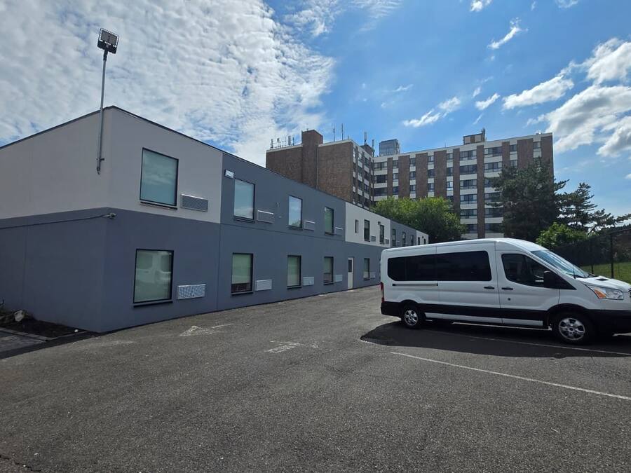 A parking lot with a white van parked in front of a modern building with multiple windows and a flat roof.