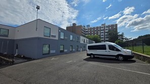 Un parcheggio con un furgone bianco parcheggiato di fronte a un edificio moderno con molte finestre e un tetto piatto.