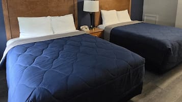 A hotel room with two beds, wooden headboards, white bedding, a bedside lamp, and a telephone on the nightstand.