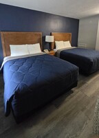 Habitación de hotel con dos camas, cabeceros de madera, ropa de cama blanca, una lámpara de noche y un teléfono en la mesita de noche.