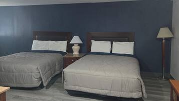 A hotel room with two beds, a nightstand, a lamp, and a window with a city view.