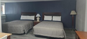 A hotel room with two beds, a nightstand, a lamp, and a window with a city view.
