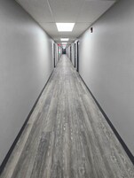 Un largo y estrecho pasillo con piso de madera y paredes grises, que conduce a una puerta al final.