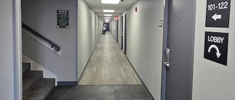 A hotel hallway with a fire safety sign, an exit sign, and directional signs to the lobby.