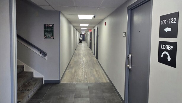 A hotel hallway with a fire safety sign, an exit sign, and directional signs to the lobby.