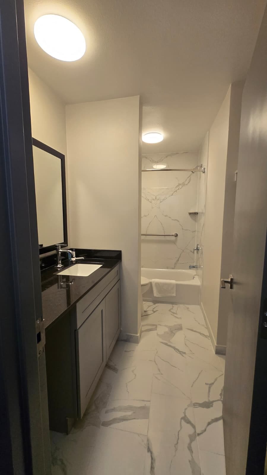A modern bathroom with a marble floor, a bathtub, and a shower area.