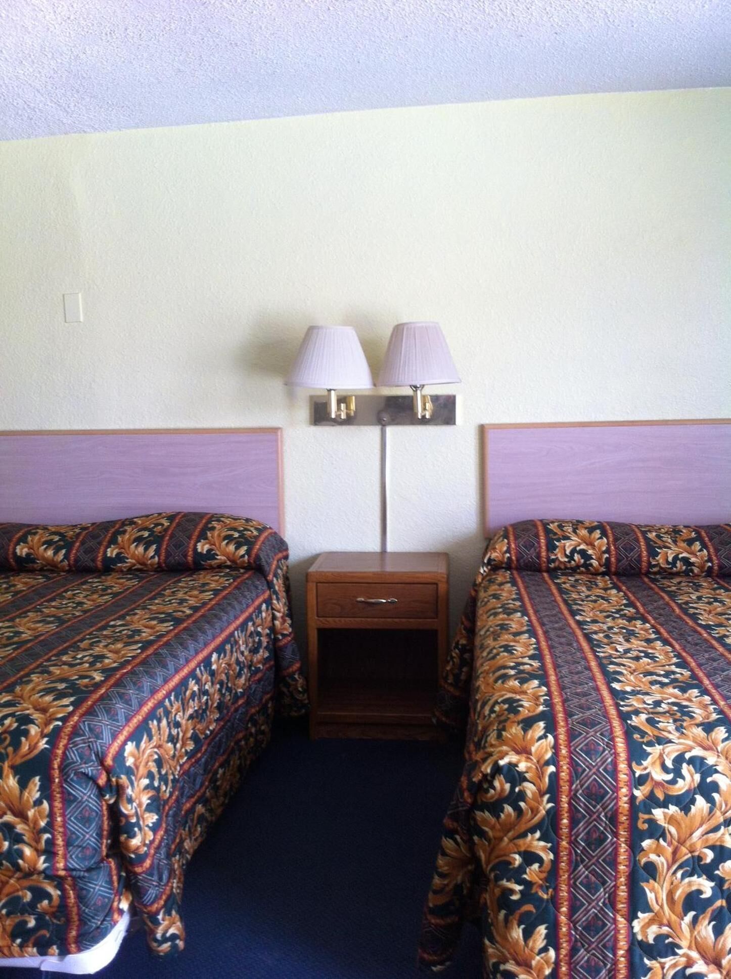 A hotel room with two beds, a nightstand, and two wall-mounted lamps.