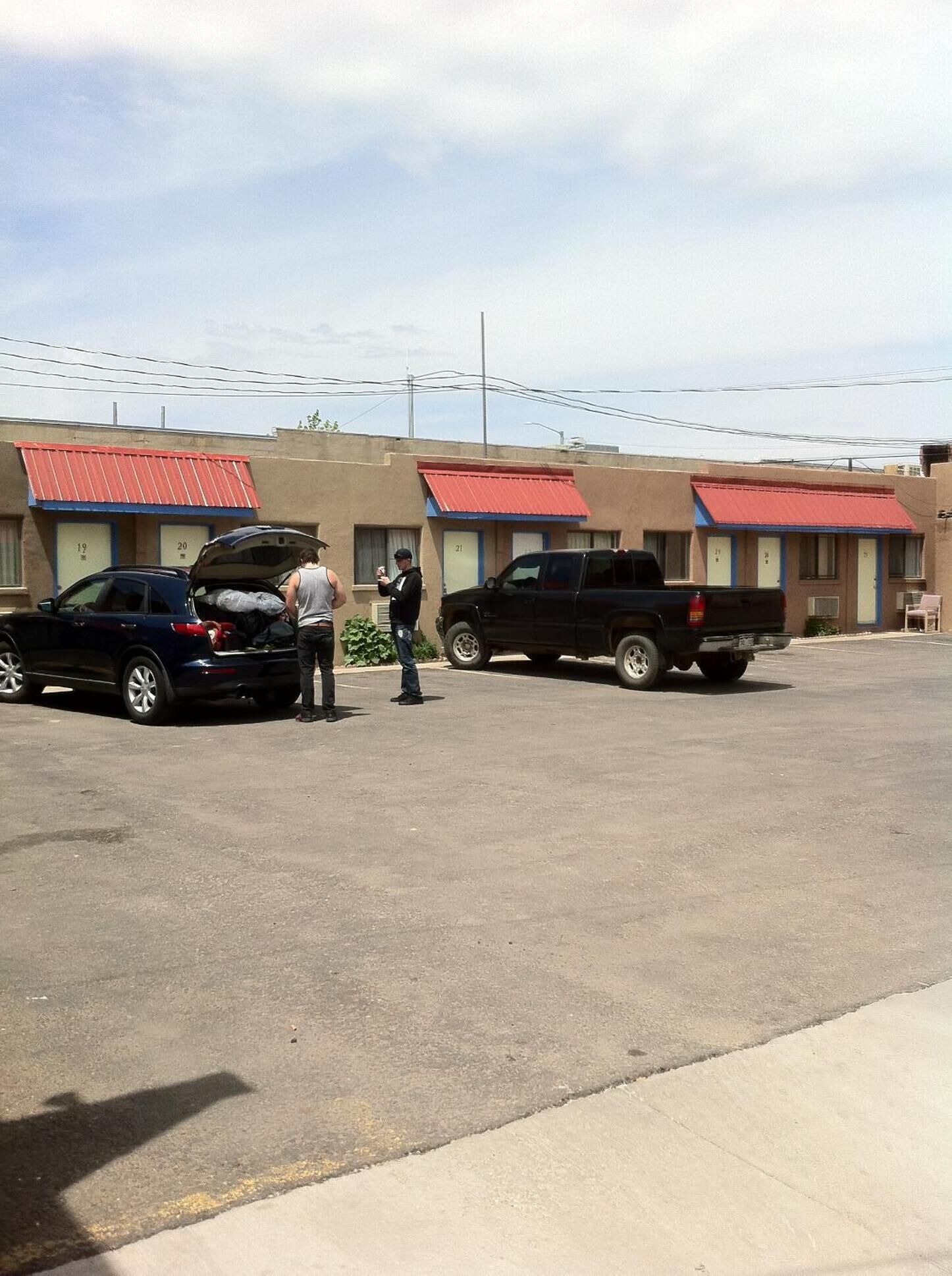 A parking lot with a row of motel buildings, each with a red awning and numbered doors.