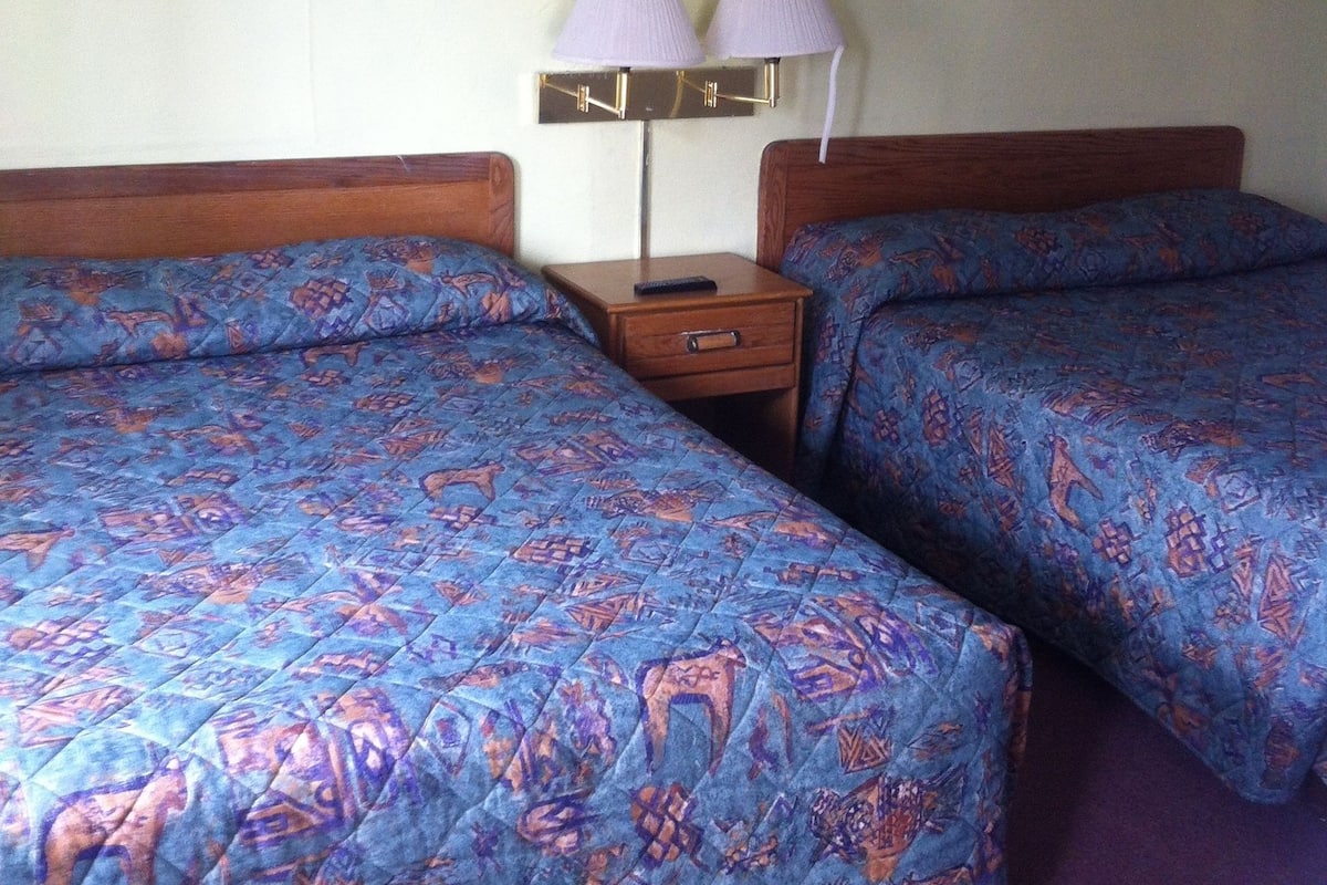 A hotel room with two beds, a nightstand, and a lamp.