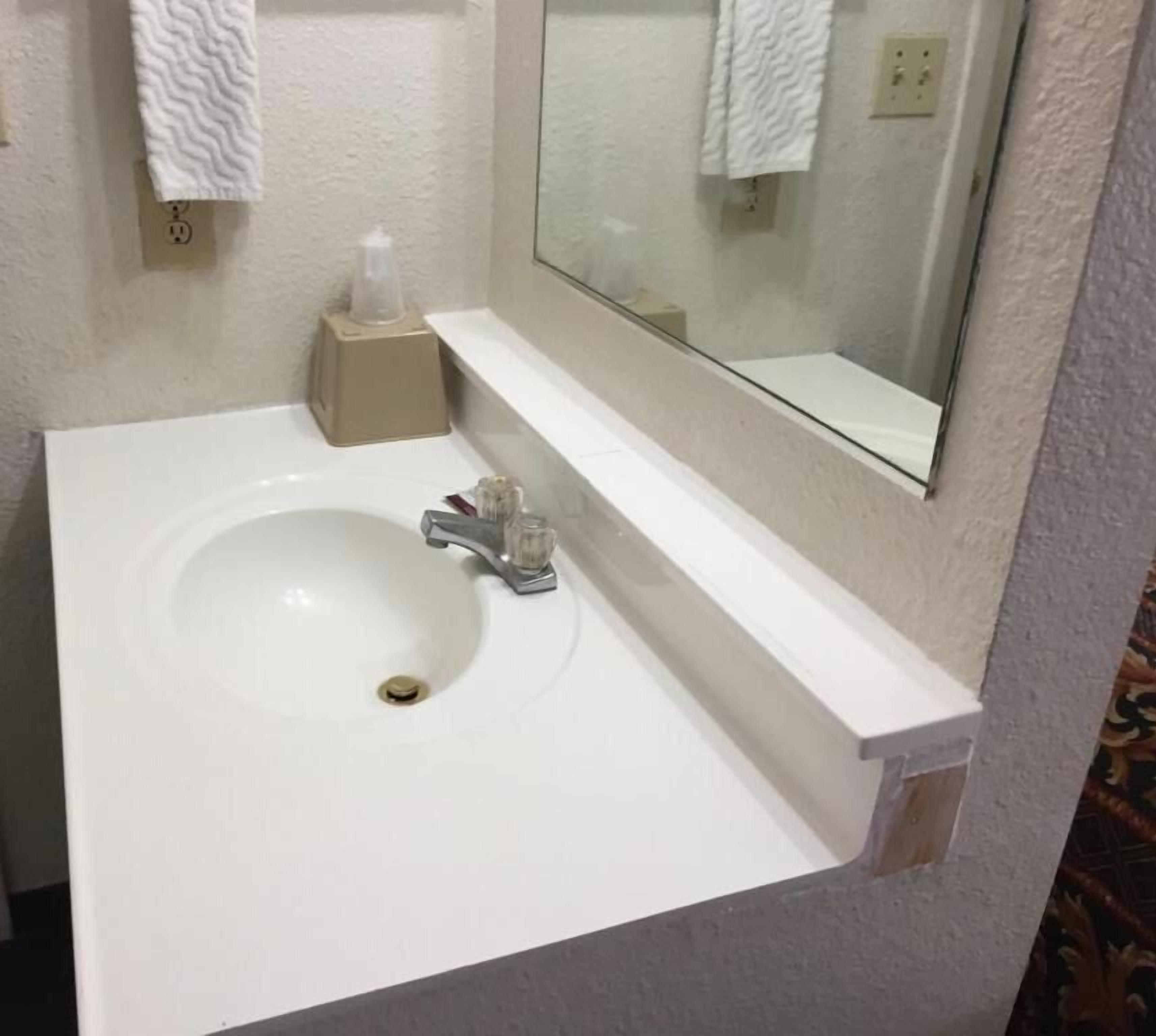 A bathroom with a white sink, a mirror, and a towel dispenser.