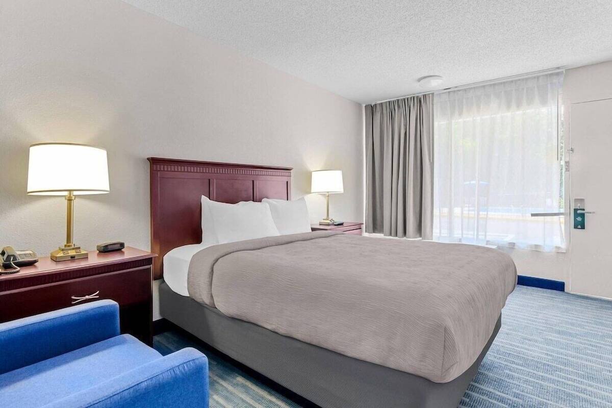 A hotel room with a large bed, two bedside tables, a desk, a chair, and a window with curtains.
