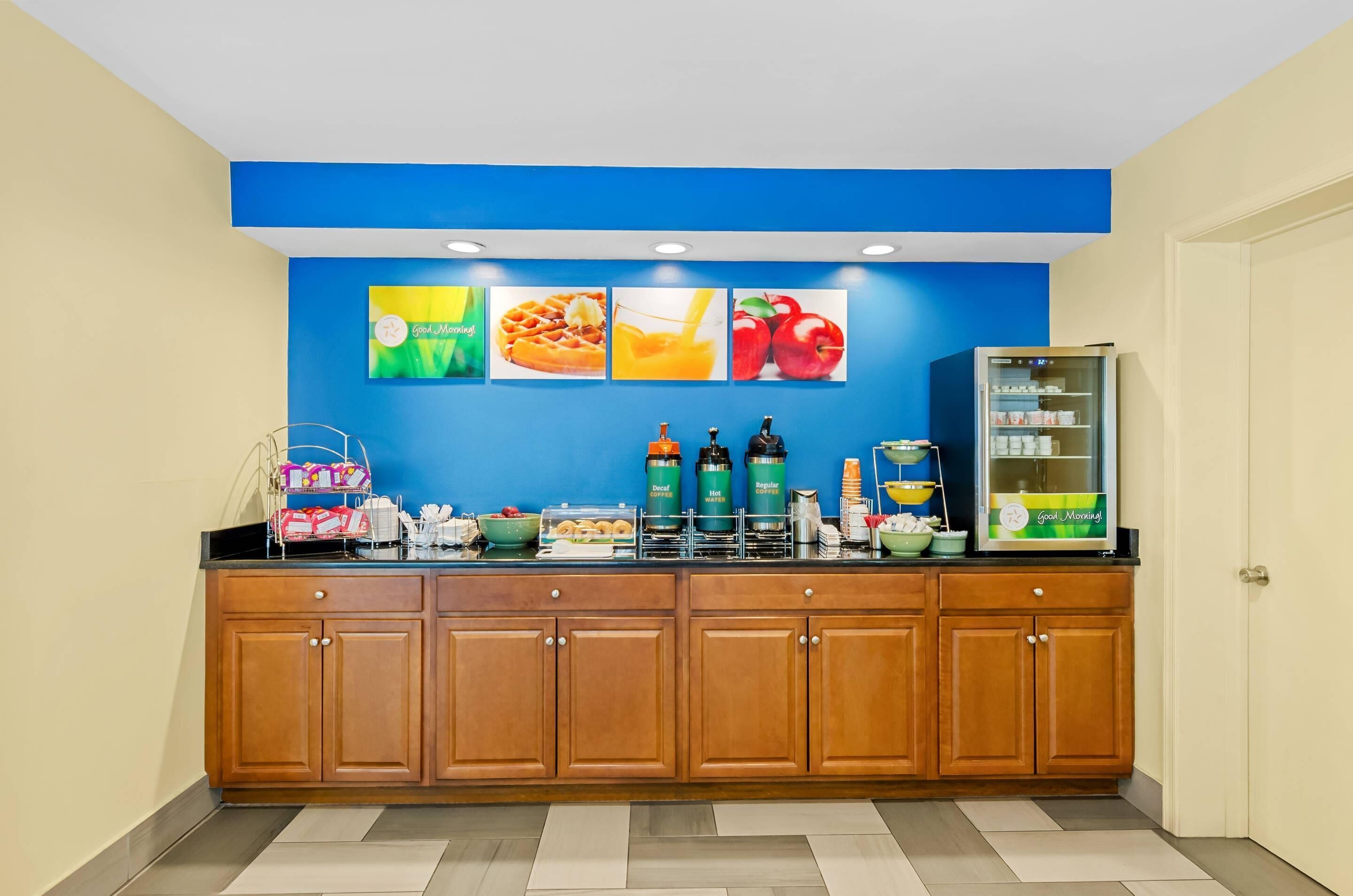A breakfast bar with a blue wall, wooden cabinets, and a refrigerator stocked with beverages.
