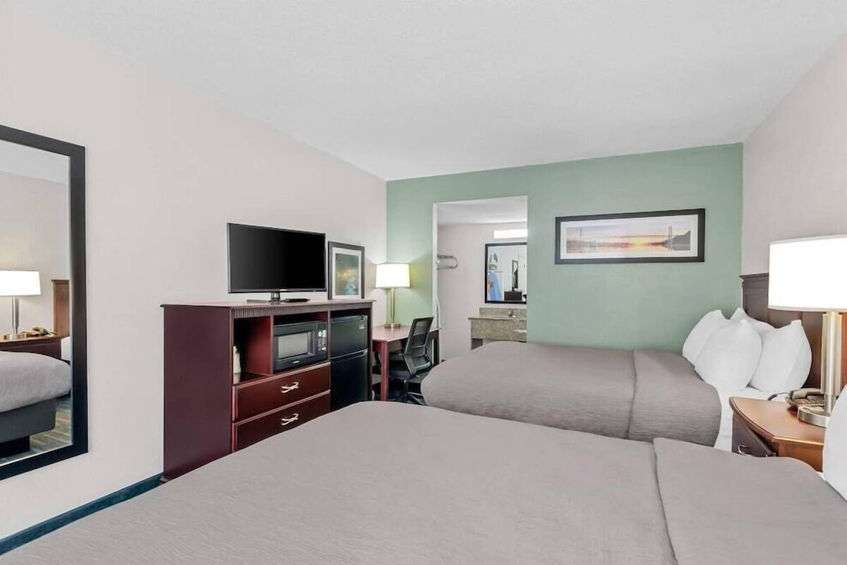 A hotel room with two beds, a TV, a desk, a chair, a mirror, and a painting on the wall.