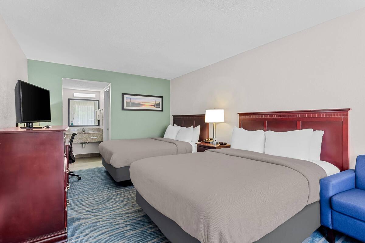 A hotel room with two beds, a desk with a TV, a desk lamp, and a chair.