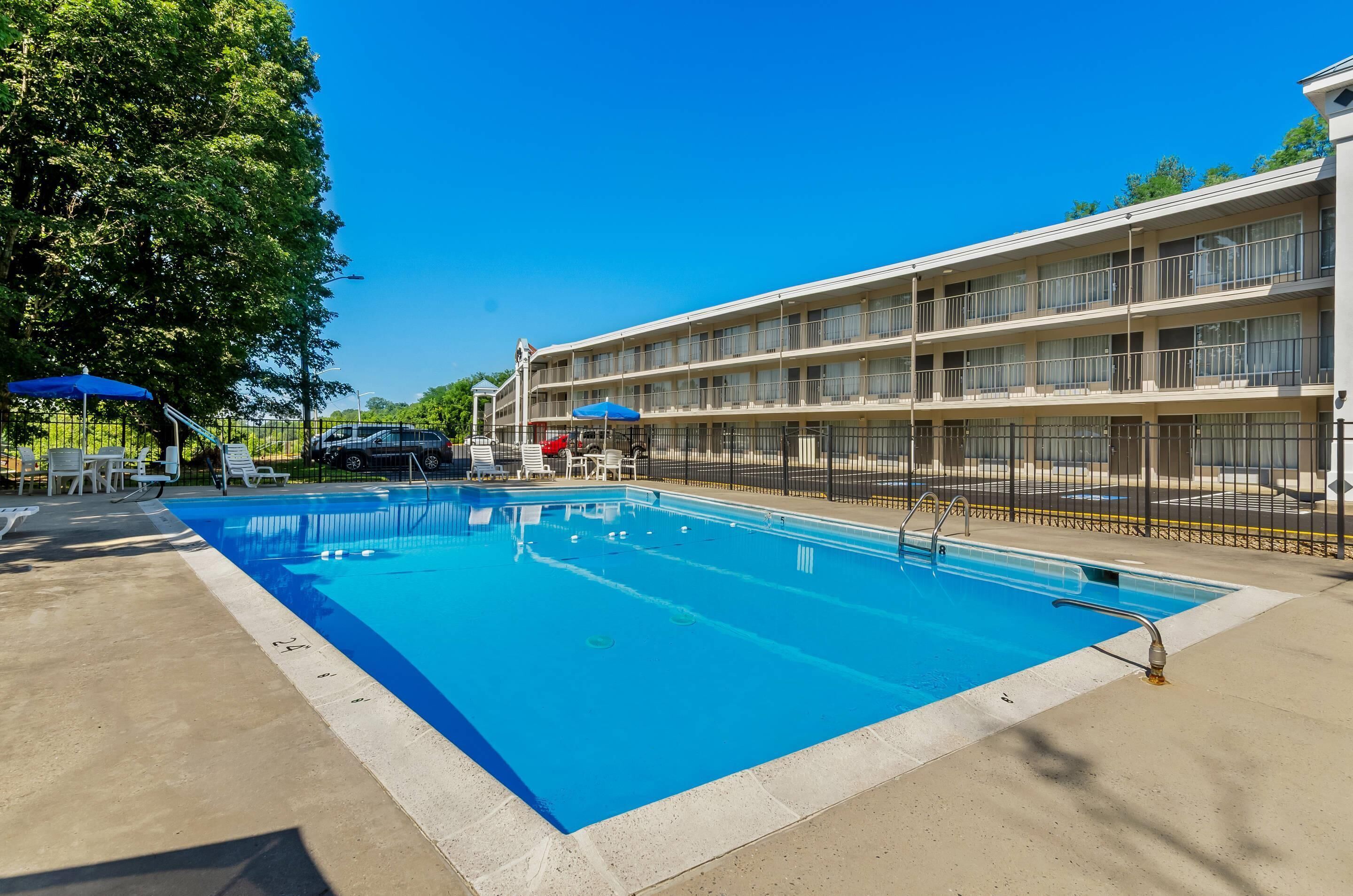 Une piscine entourée d’une clôture, des chaises longues et un immeuble à plusieurs étages doté de balcons.