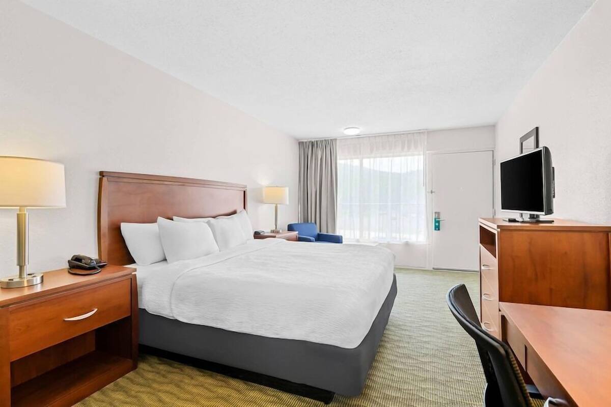 A hotel room with a bed, bedside tables, a desk, a chair, a television, and a window with curtains.