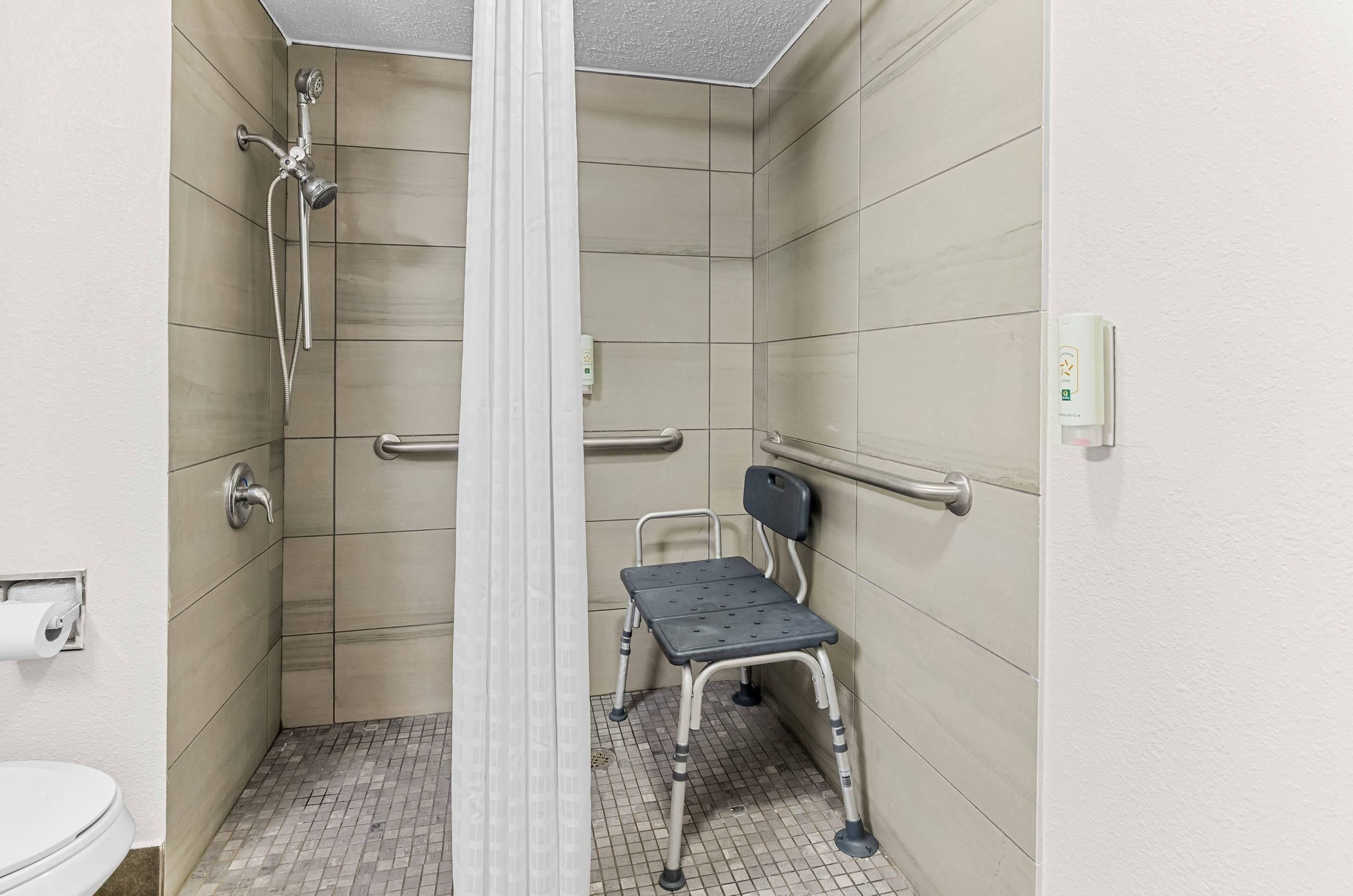 A small, tiled bathroom with a shower, a toilet, and a wheelchair-accessible bench.
