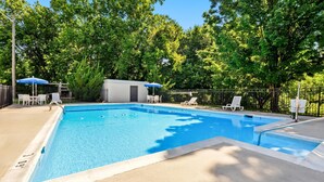Una piscina rectangular con solárium de hormigón, rodeada de árboles y una valla metálica.
