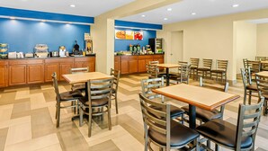 Un comedor con varias mesas y sillas, una cocina con diferentes electrodomésticos, y una pared azul decorativa.