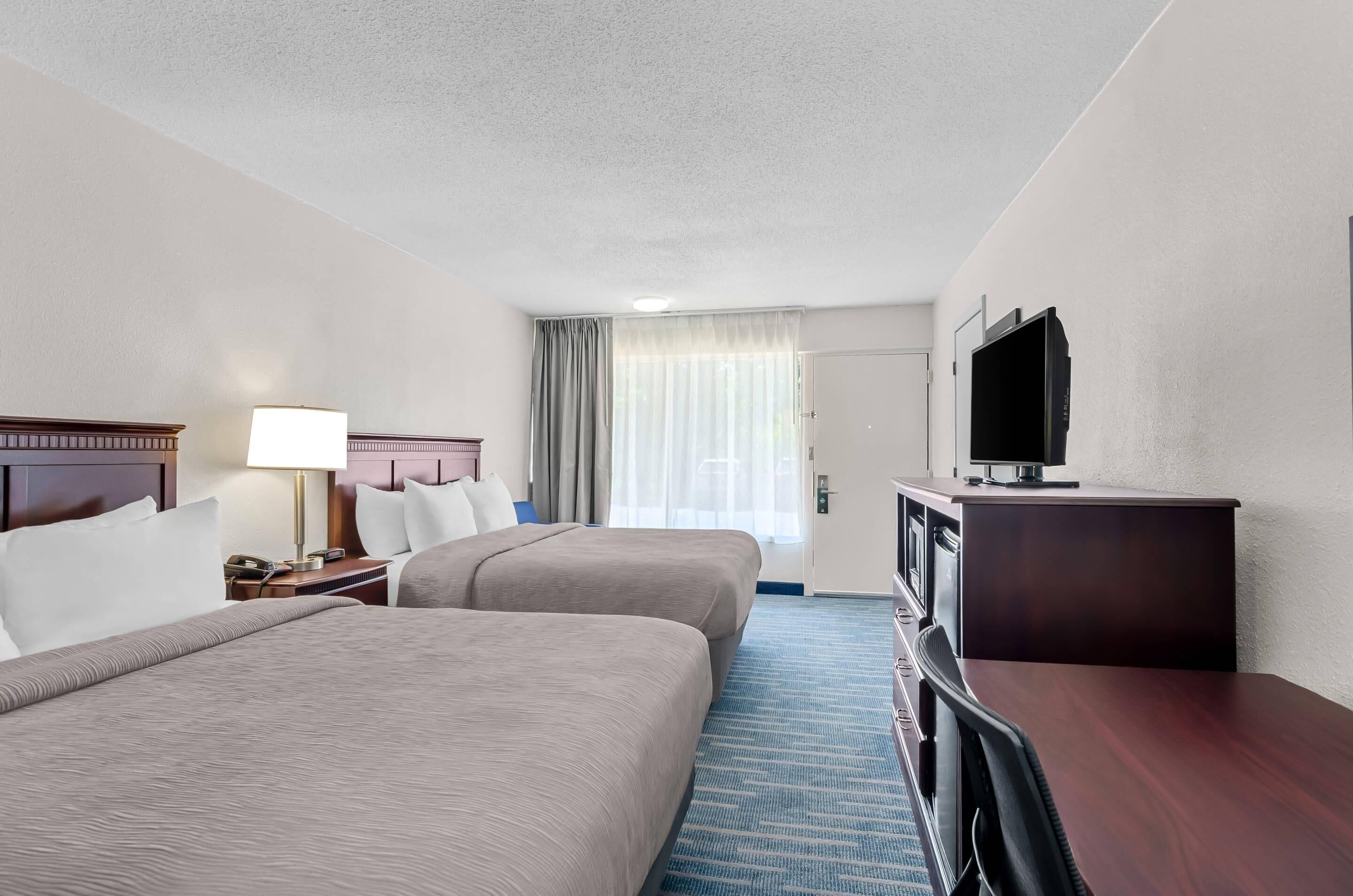 A hotel room with two beds, a desk, a television, and a window with curtains.