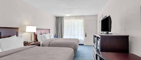 A hotel room with two beds, a desk, a television, and a window with curtains.