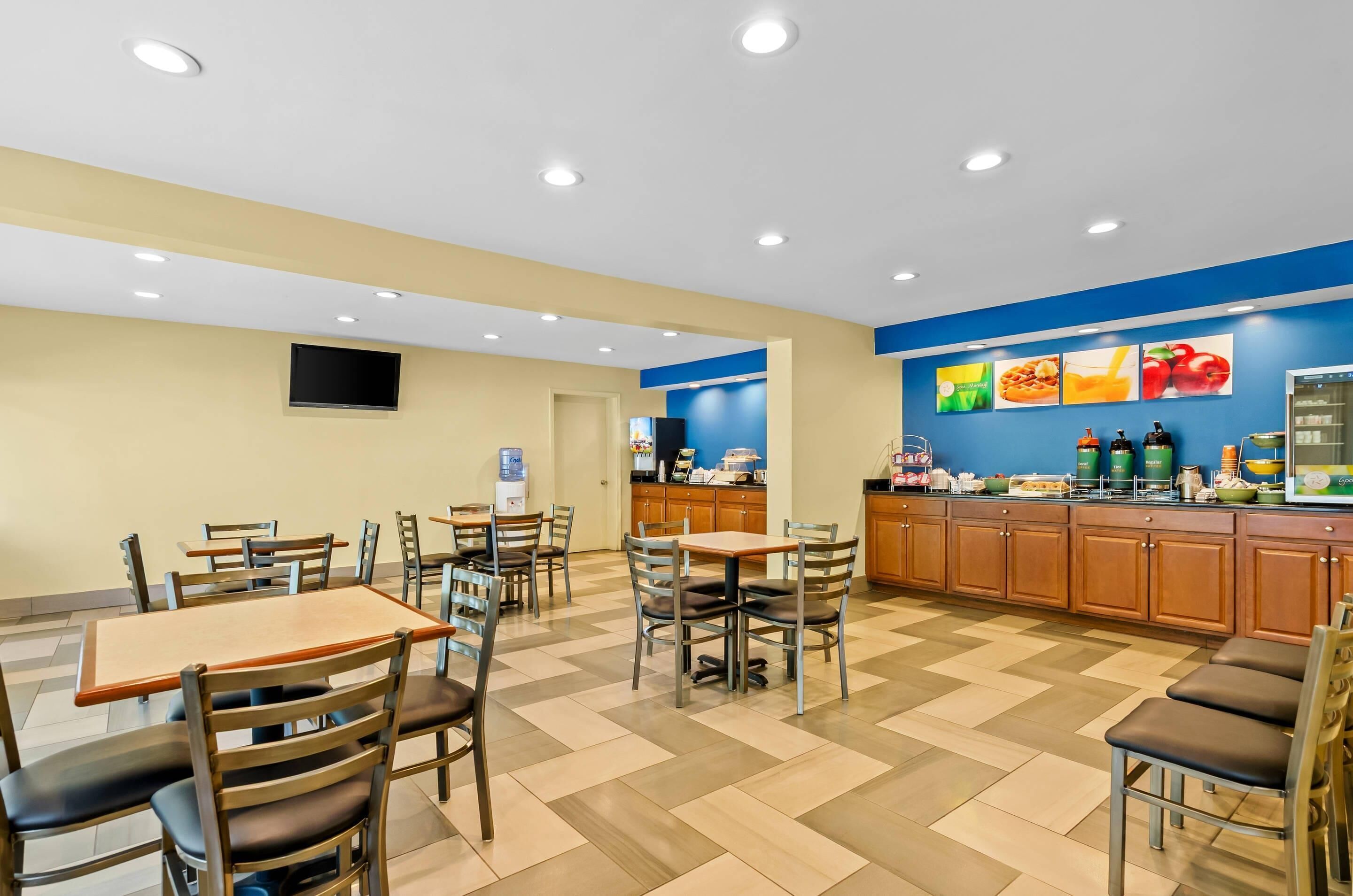 Un restaurante con varias mesas y sillas, una barra con alimentos y una pared decorada con imágenes de frutas y bebidas.