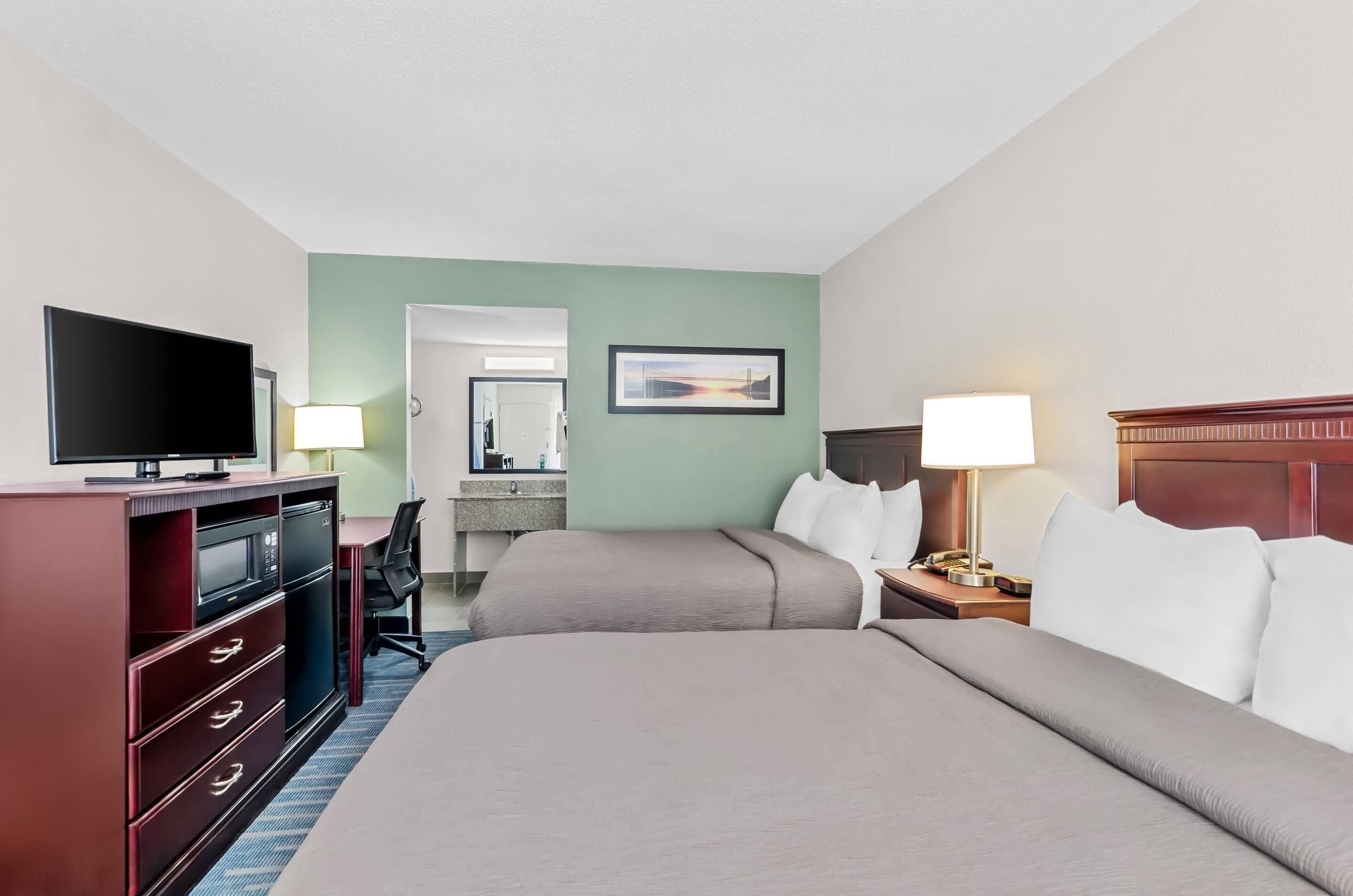 A hotel room with two beds, a TV, a desk, a lamp, and a painting on the wall.