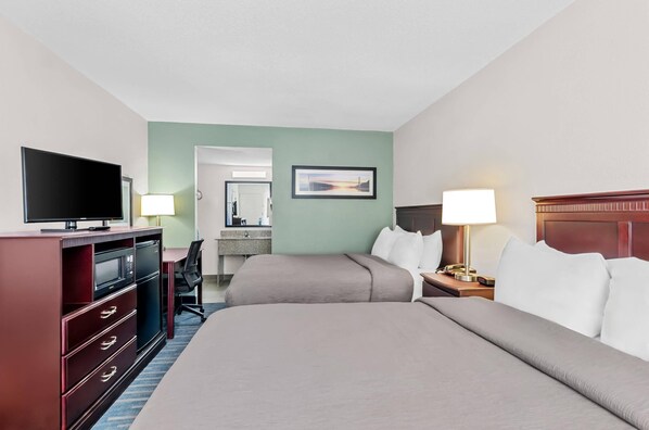 A hotel room with two beds, a TV, a desk, a lamp, and a painting on the wall.