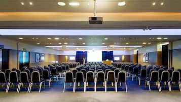 A conference room with rows of chairs, a podium, and a projector on the ceiling.