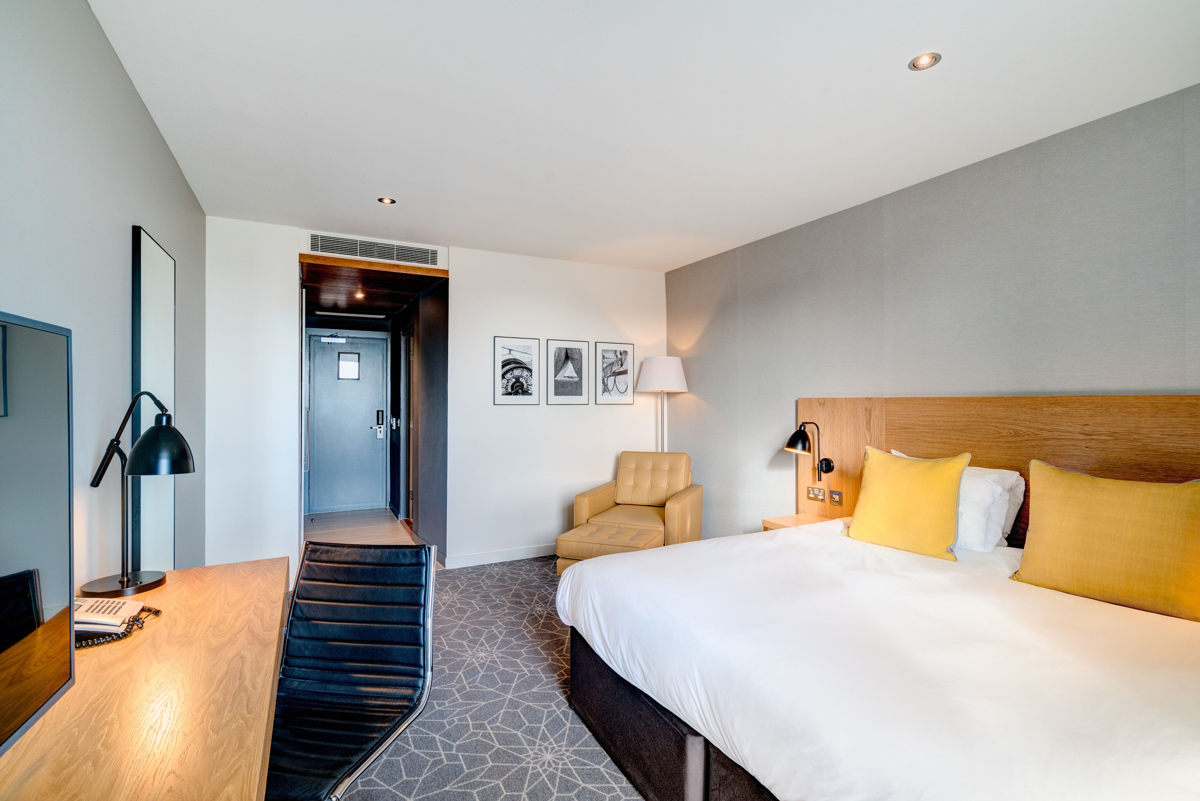 A modern hotel room with a bed, a chair, a desk, and a staircase.