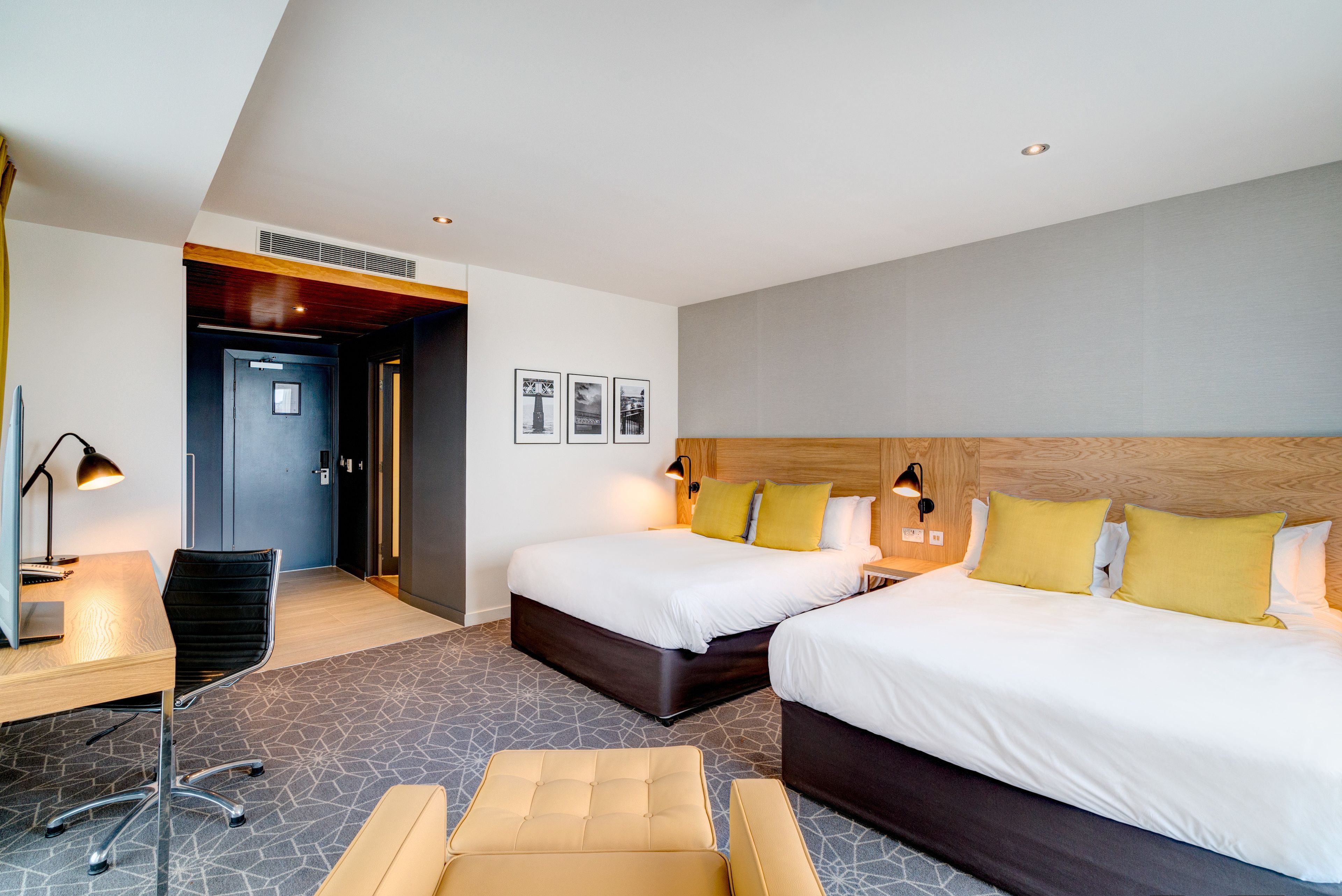 A hotel room with two beds, a desk, a chair, and a small seating area.